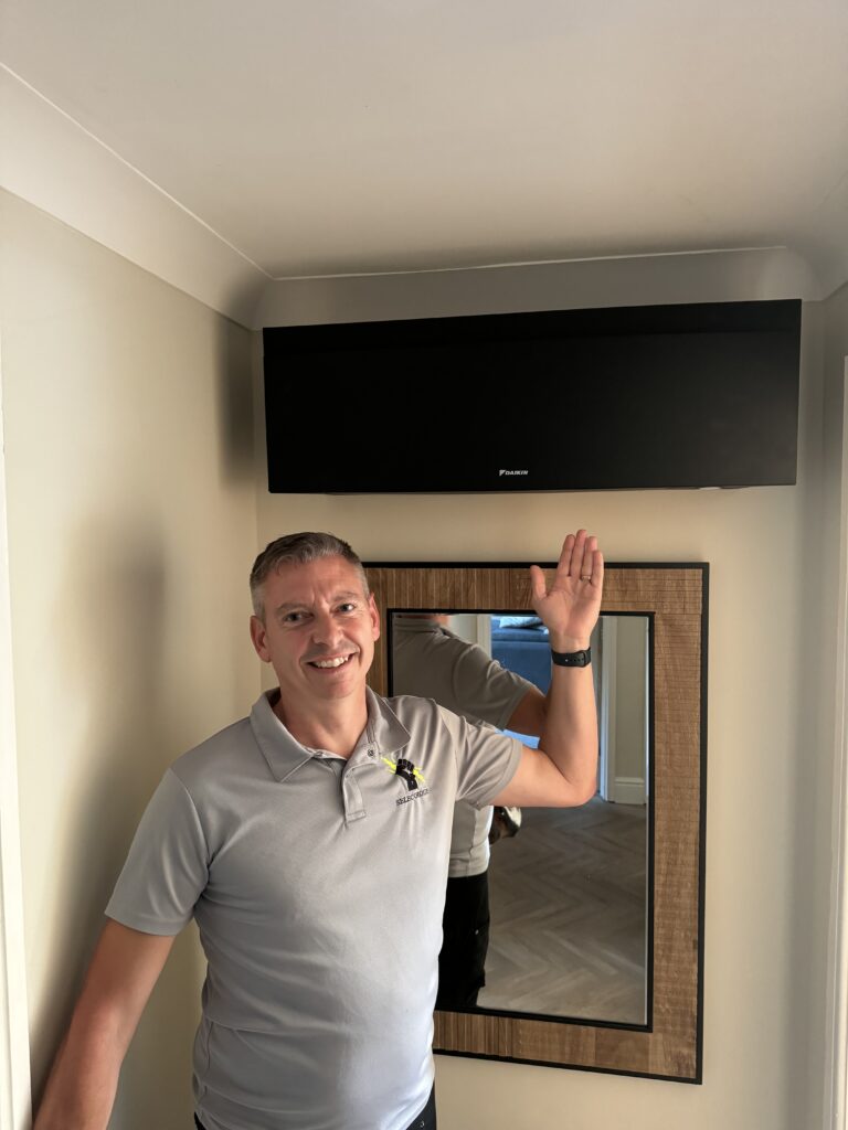 Jason Pope beside a black wall mounted air conditioning unit he installed