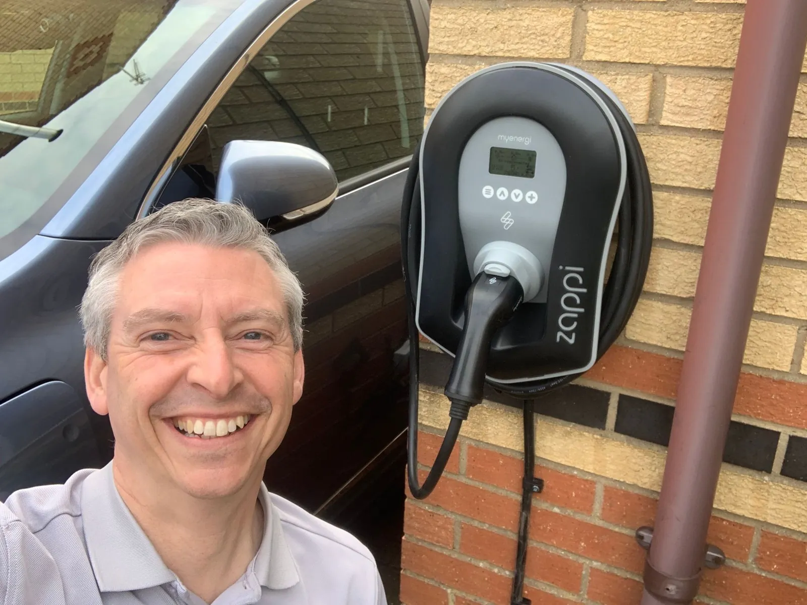 Jason Pope of Selec Group beside a newly fitted myenergi zappi EV charger on a brick wall