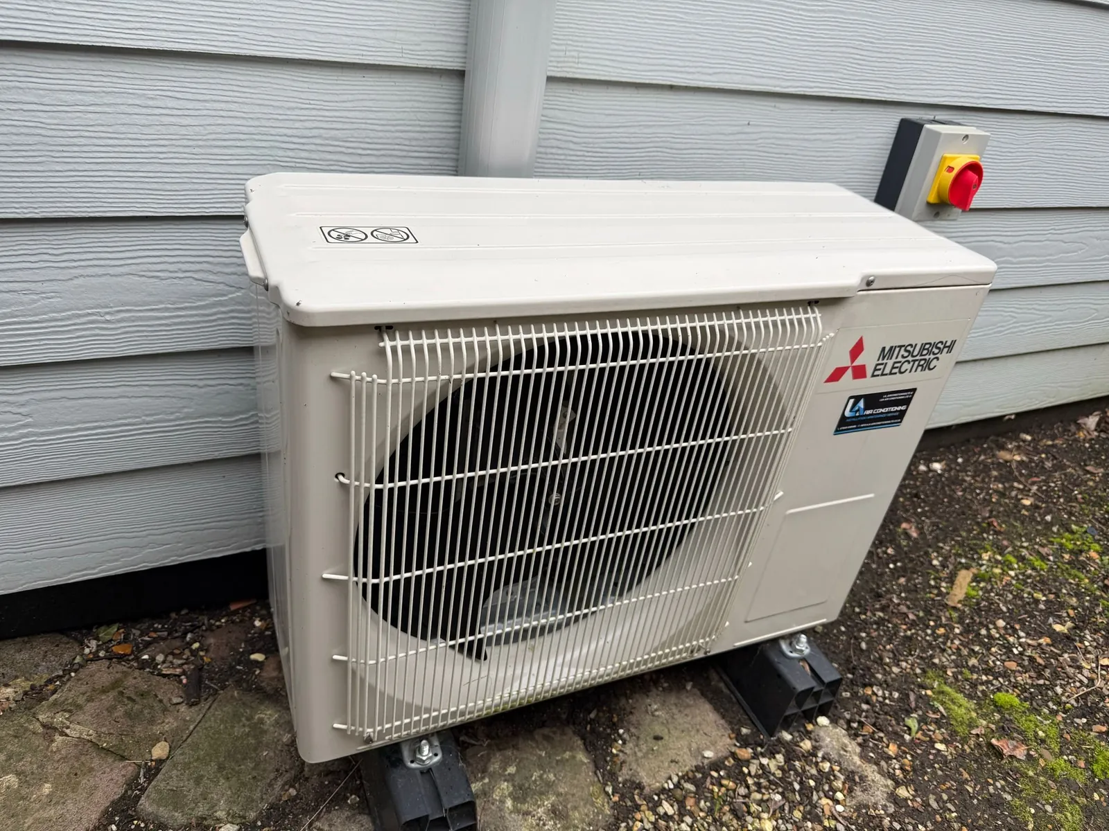 Mitsubishi air conditioning outdoor unit on anti vibration feet beside a house, installed by Selec Group
