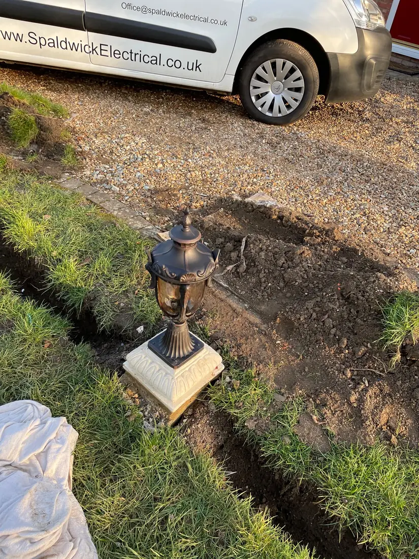 Garden post lantern being installed with the cable trench still open and a Spaldwick Electrical van behind