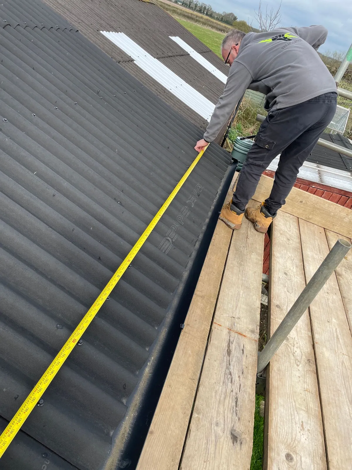 Selec Group team member measuring a roof from the scaffold at the start of an install