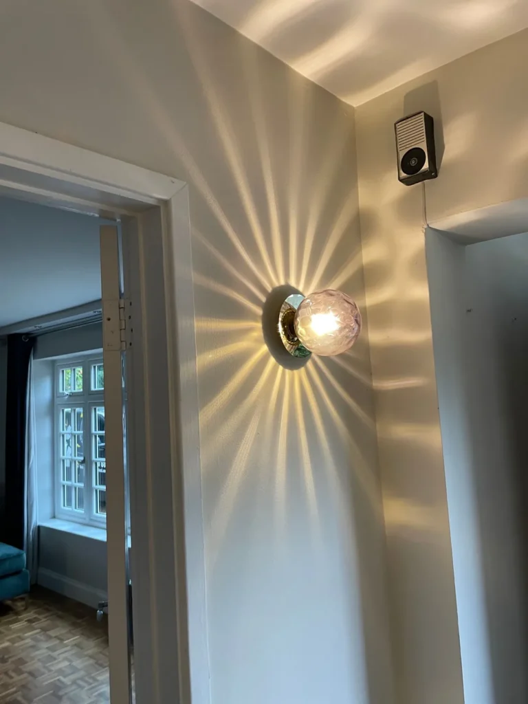 Glass wall light casting a starburst pattern in a hallway, fitted by Selec Group