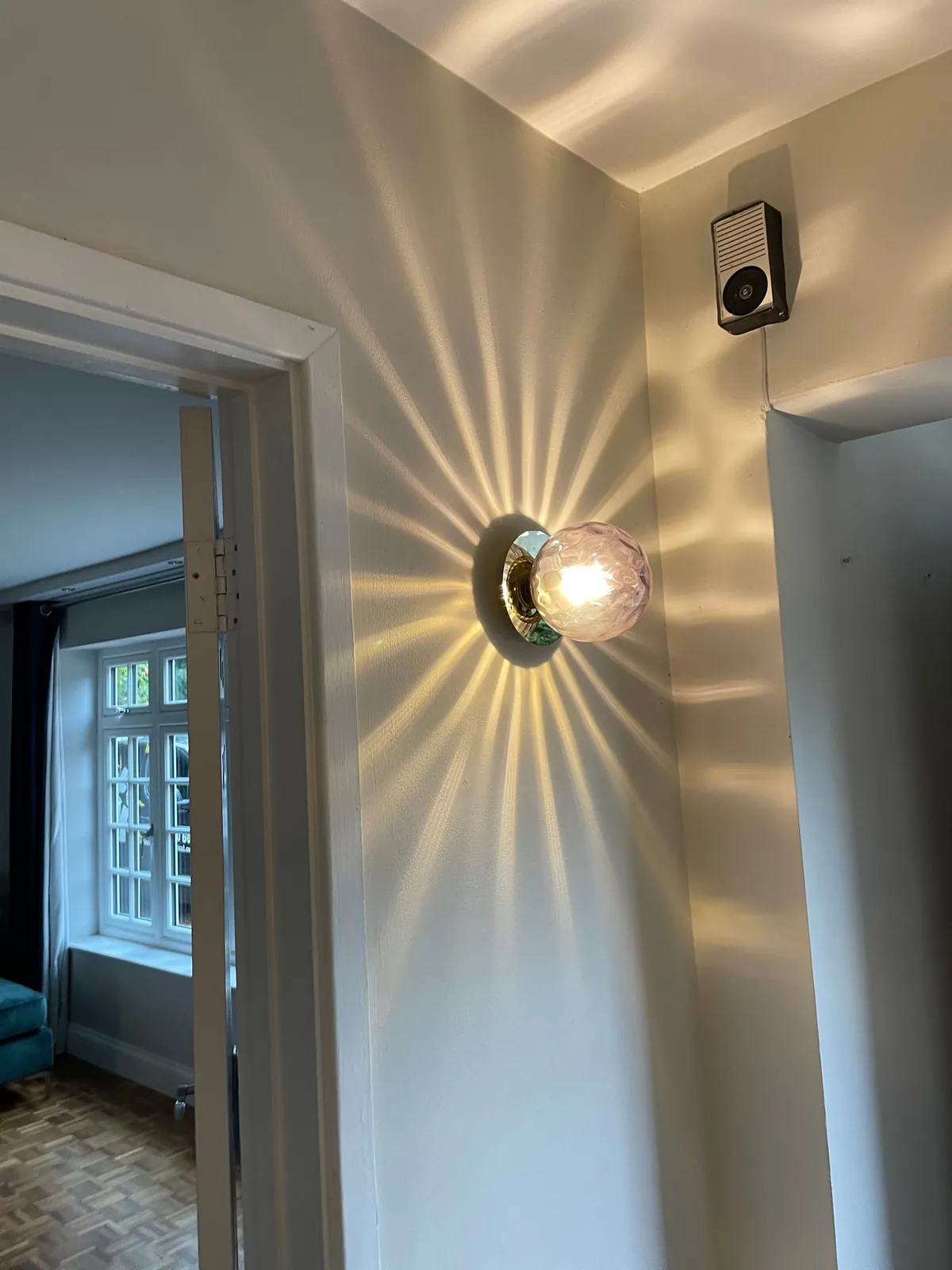 Glass wall light casting a starburst pattern in a hallway, fitted by Selec Group
