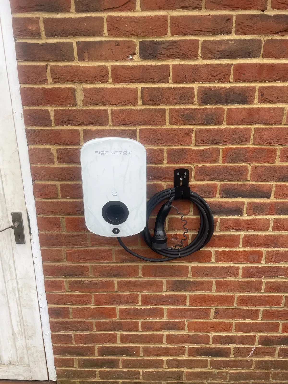 White EV charger on a red brick wall, installed by Selec Group